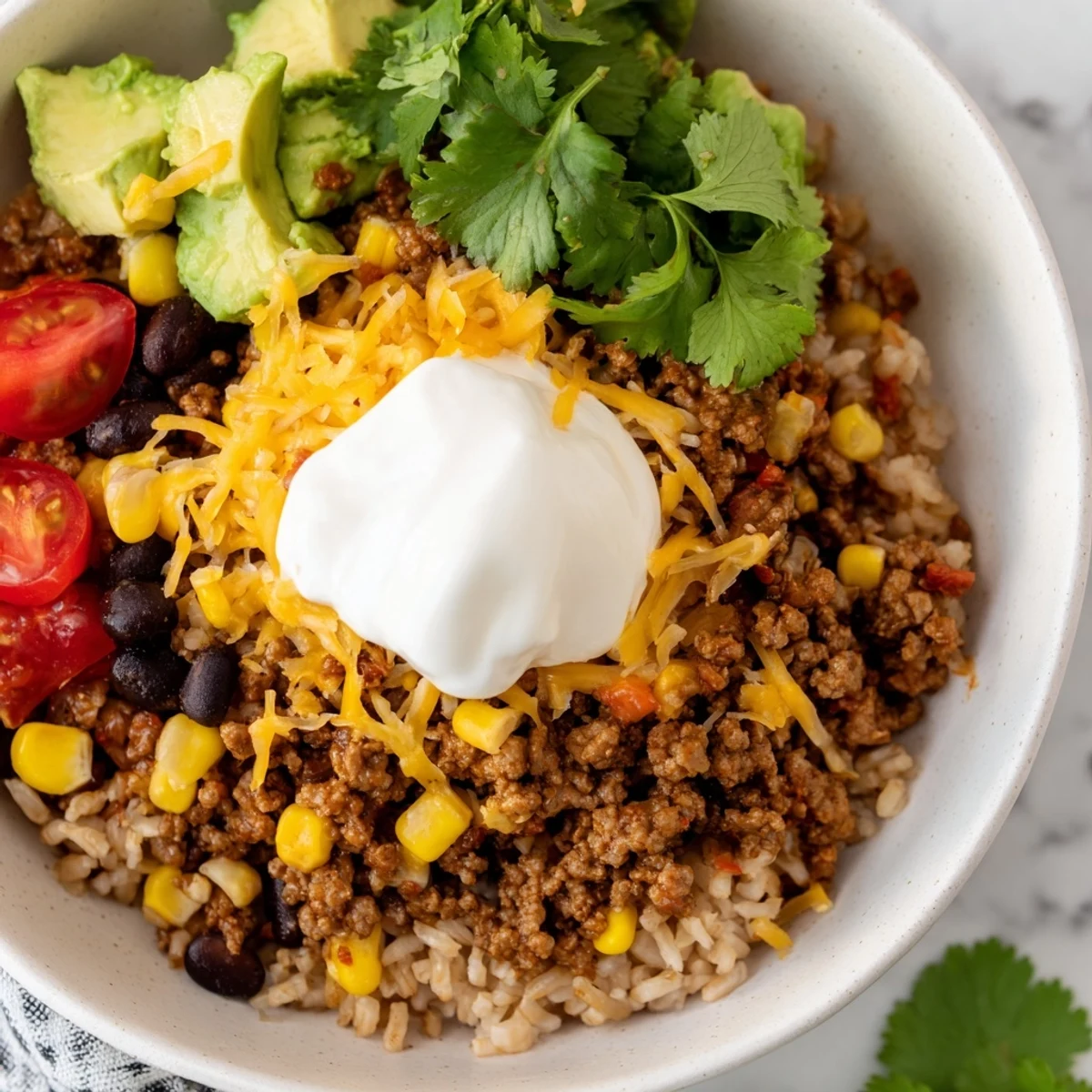 Seasoned ground beef and fluffy brown rice topped with avocado, cheese, and sour cream in a hearty Beef Burrito Bowl.