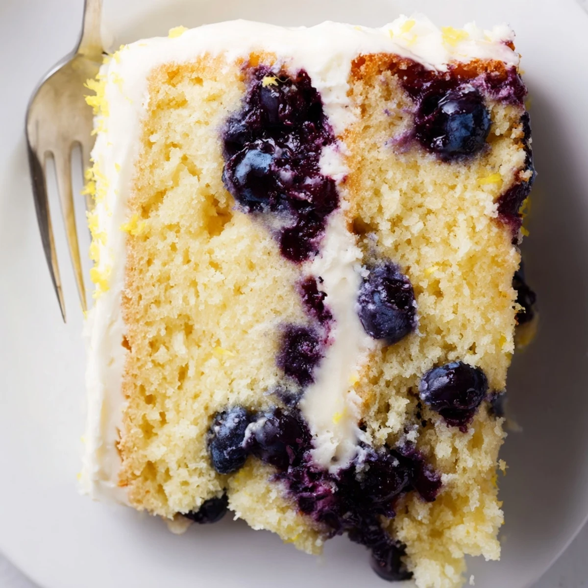 Slice of zesty Lemon Blueberry Cake with creamy frosting on a dessert plate, ready to serve.