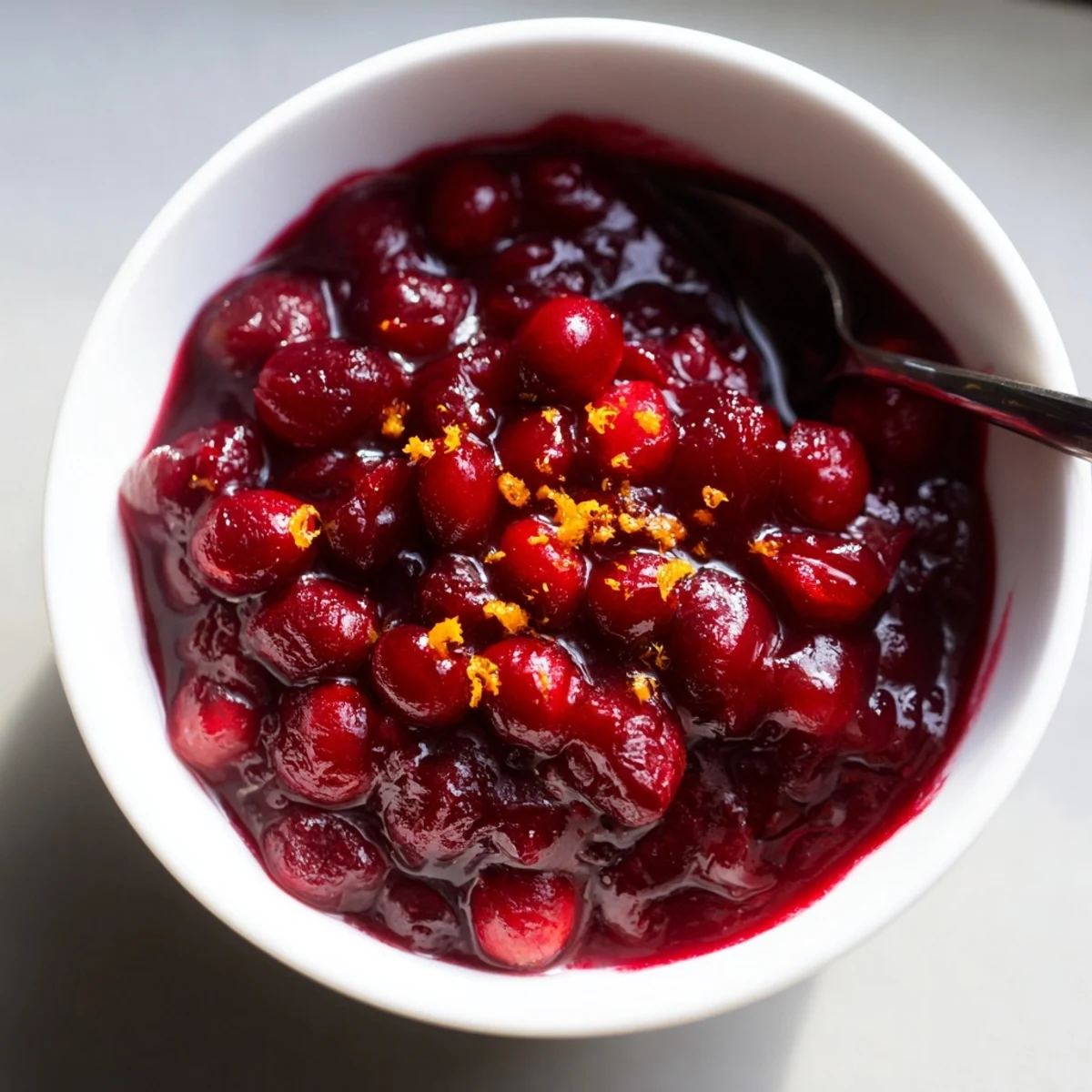 Vibrant homemade Cranberry Sauce with Orange Juice garnished with orange zest, beside golden roast turkey for a festive meal.