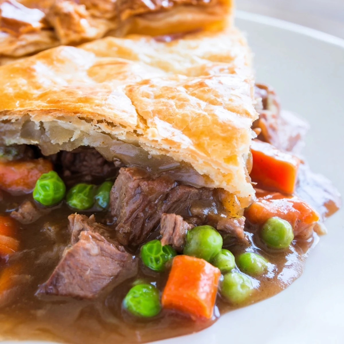 A slice of hearty Beef Pie with Flaky Crust on a plate, served alongside creamy mashed potatoes and a glass of deep red wine.
