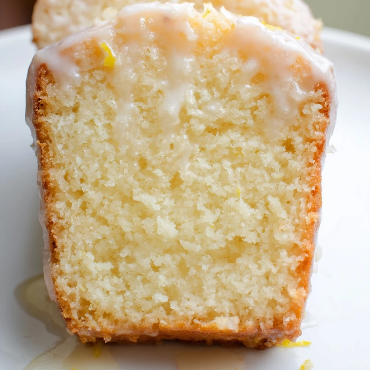 A freshly baked Lemon Loaf Cake with a glossy lemon glaze dripping down the moist, tender crumb, served on a rustic wooden board.