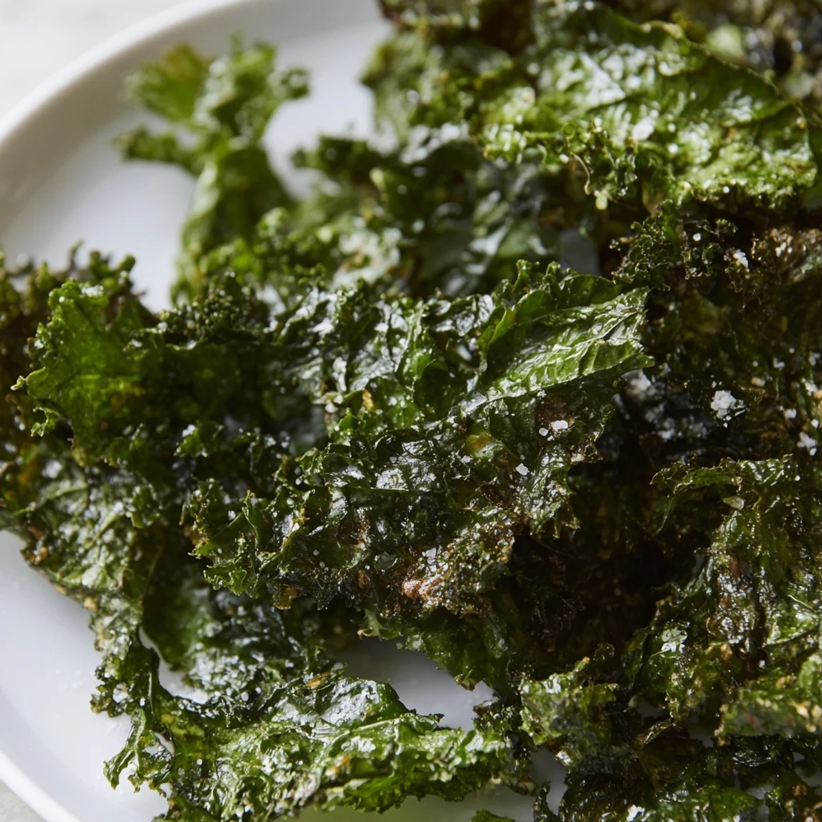 Crispy, oven-baked green kale chips with sea salt arranged on a parchment-lined baking sheet, with a bowl of raw kale nearby.  