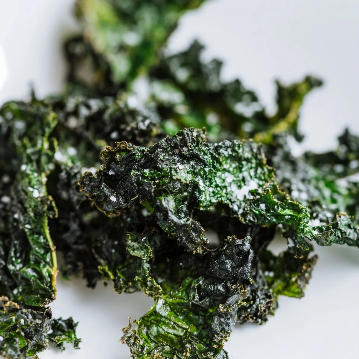 A close-up of golden-edged green kale chips with sea salt, ready to be served as a healthy vegan snack.  