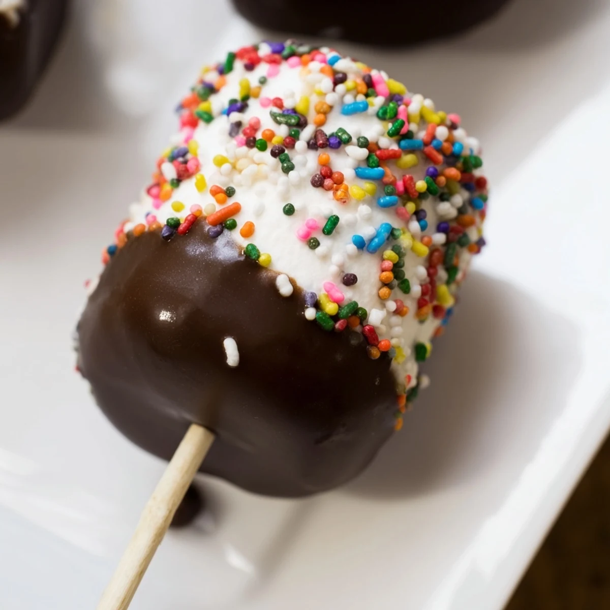 A close-up of chocolate dipped marshmallows with sprinkles, showcasing glossy coating and a soft, pillowy interior texture.