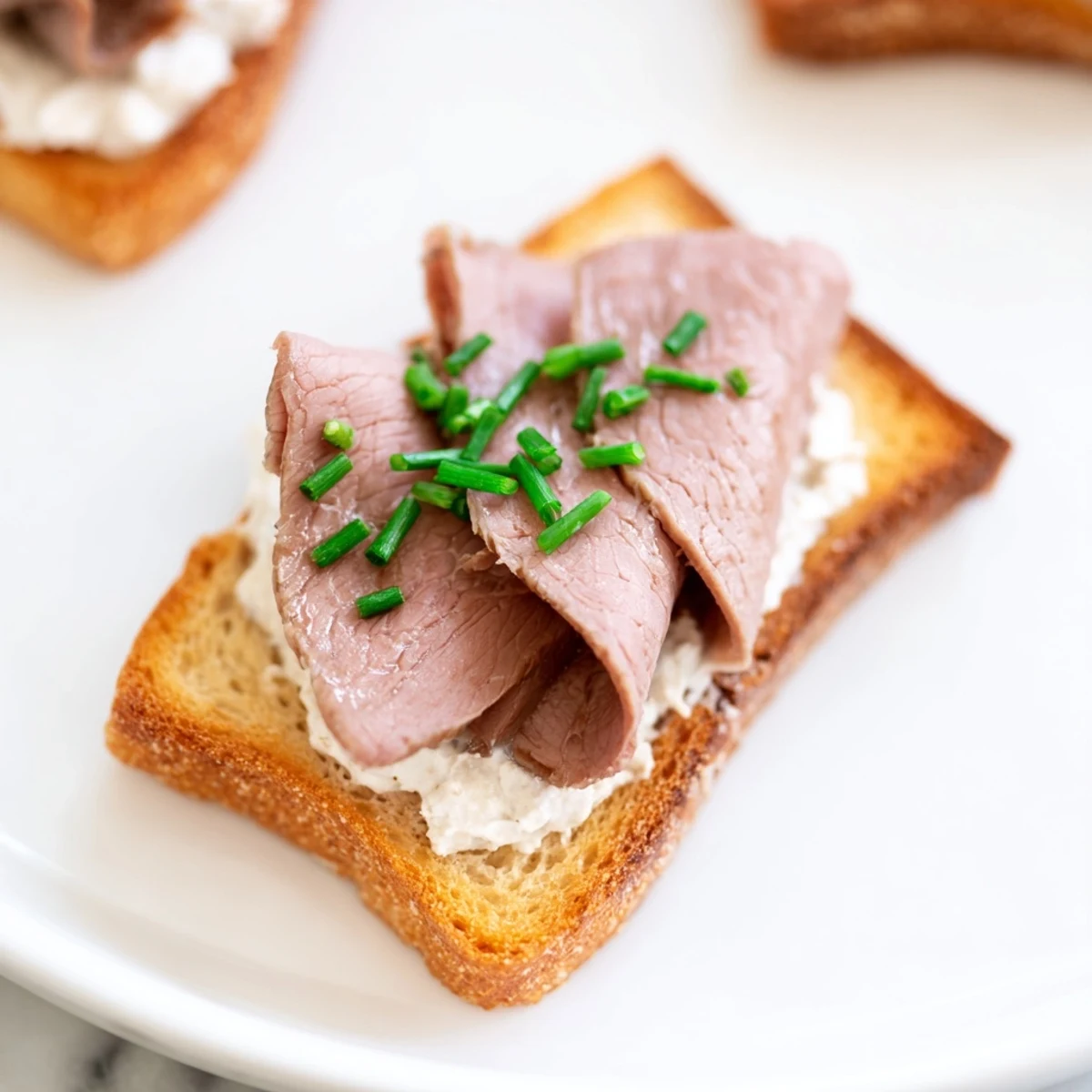 Crispy toast points topped with tender roast beef and creamy horseradish spread, garnished with fresh chives for a perfect party appetizer.  