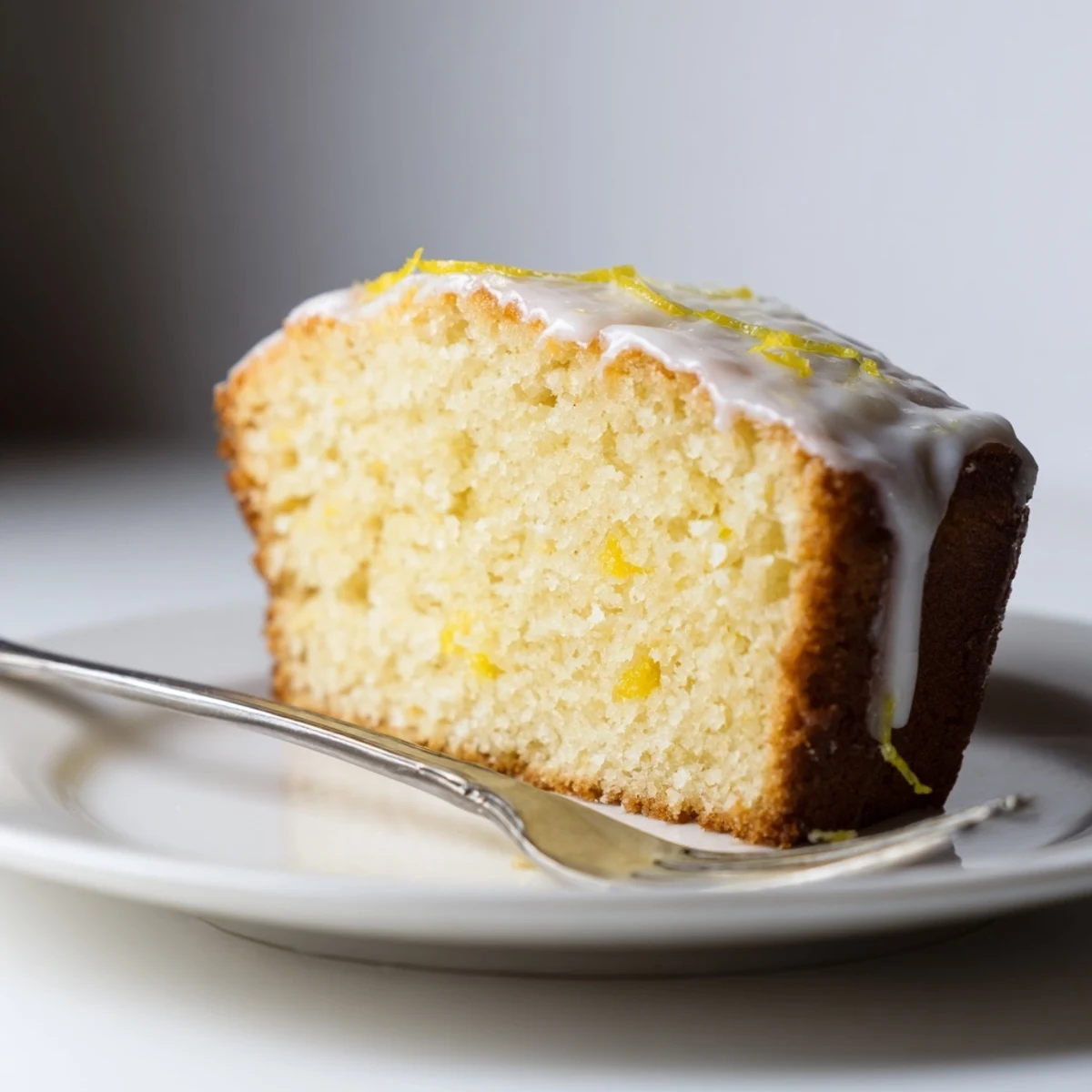 Freshly baked lemon bread loaf cut into a thick slice, revealing a moist crumb with a drizzle of sweet glaze.