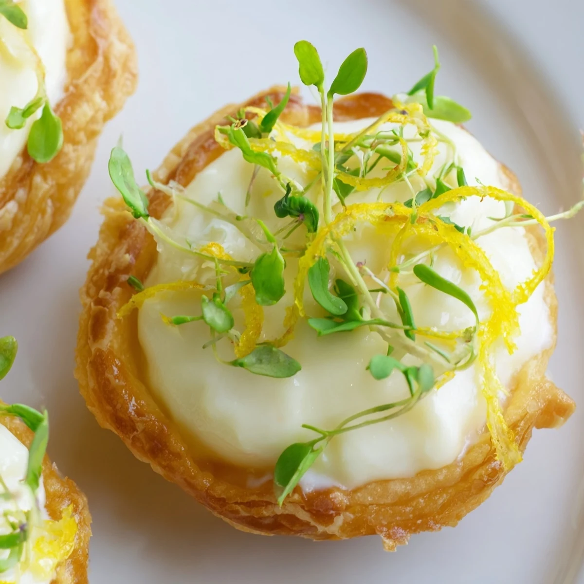 Ready-to-serve Lemon Appetizer Tartlets with lemon zest curls and a dollop of creamy filling, perfect for elegant parties.
