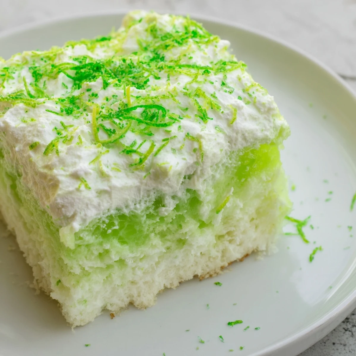 A chilled slice of St. Patricks Day Lime Poke Cake on a plate, garnished with fresh lime zest and sparkling green sprinkles.
