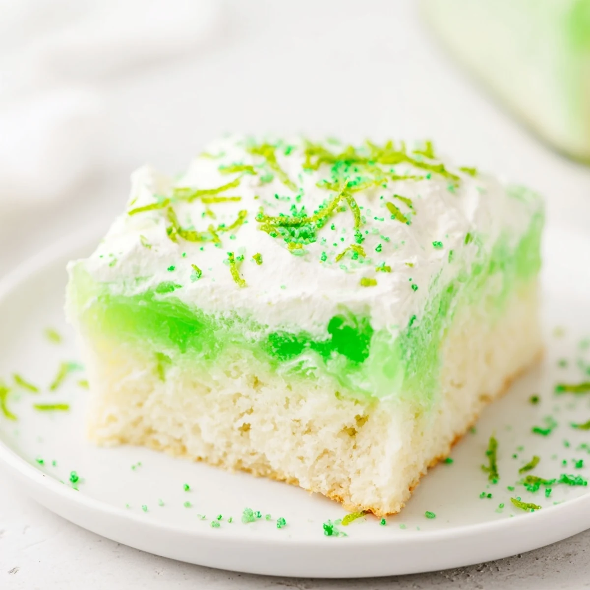Decadent St. Patricks Day Lime Poke Cake served from a glass baking dish, featuring a moist crumb and a fluffy vanilla pudding frosting.