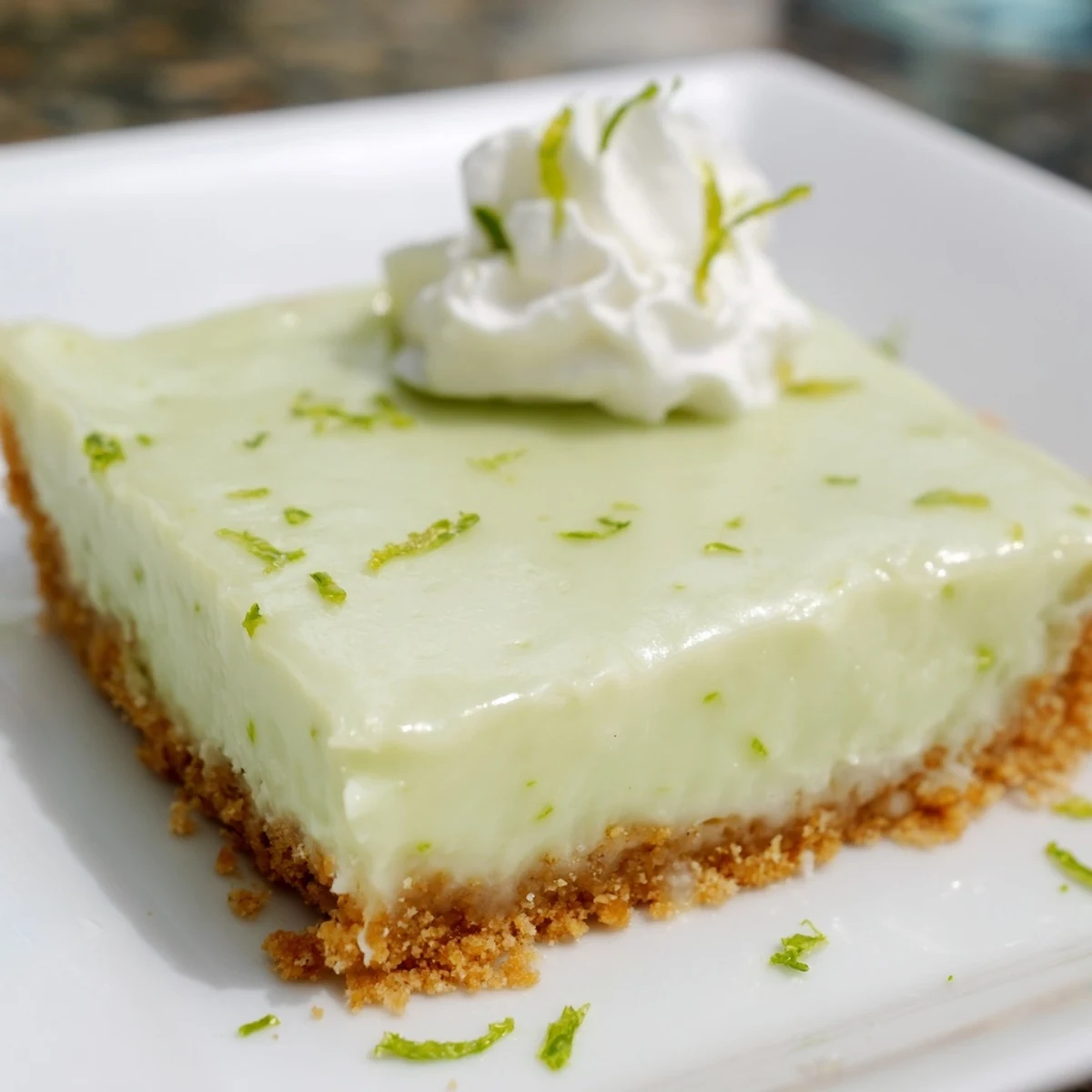 Golden-brown graham cracker crust topped with creamy key lime pie bars, garnished with fresh lime zest on a rustic wooden table.  