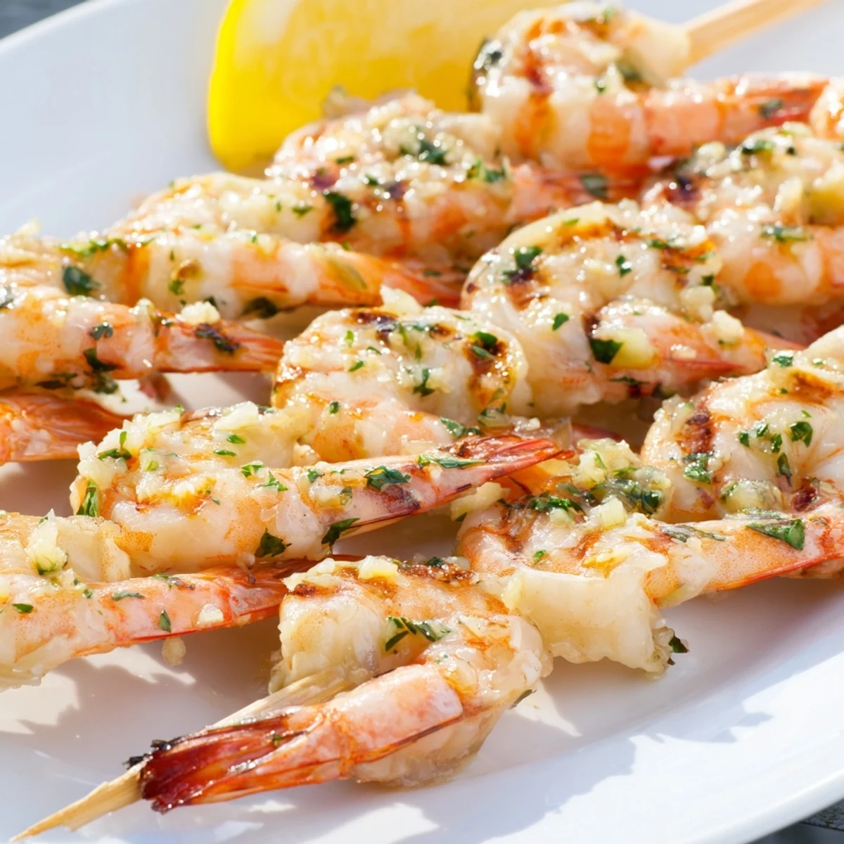 Tender Lemon Garlic Shrimp Skewers served on a white platter with fresh parsley and lemon wedges.