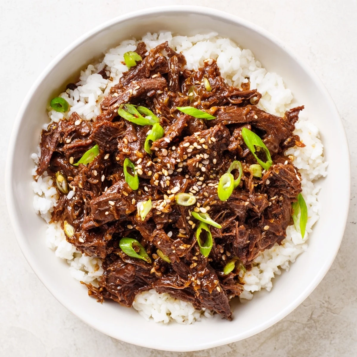 Slow-cooked tender shredded beef in savory-sweet Korean sauce, garnished with green onions and sesame seeds over steamed rice.