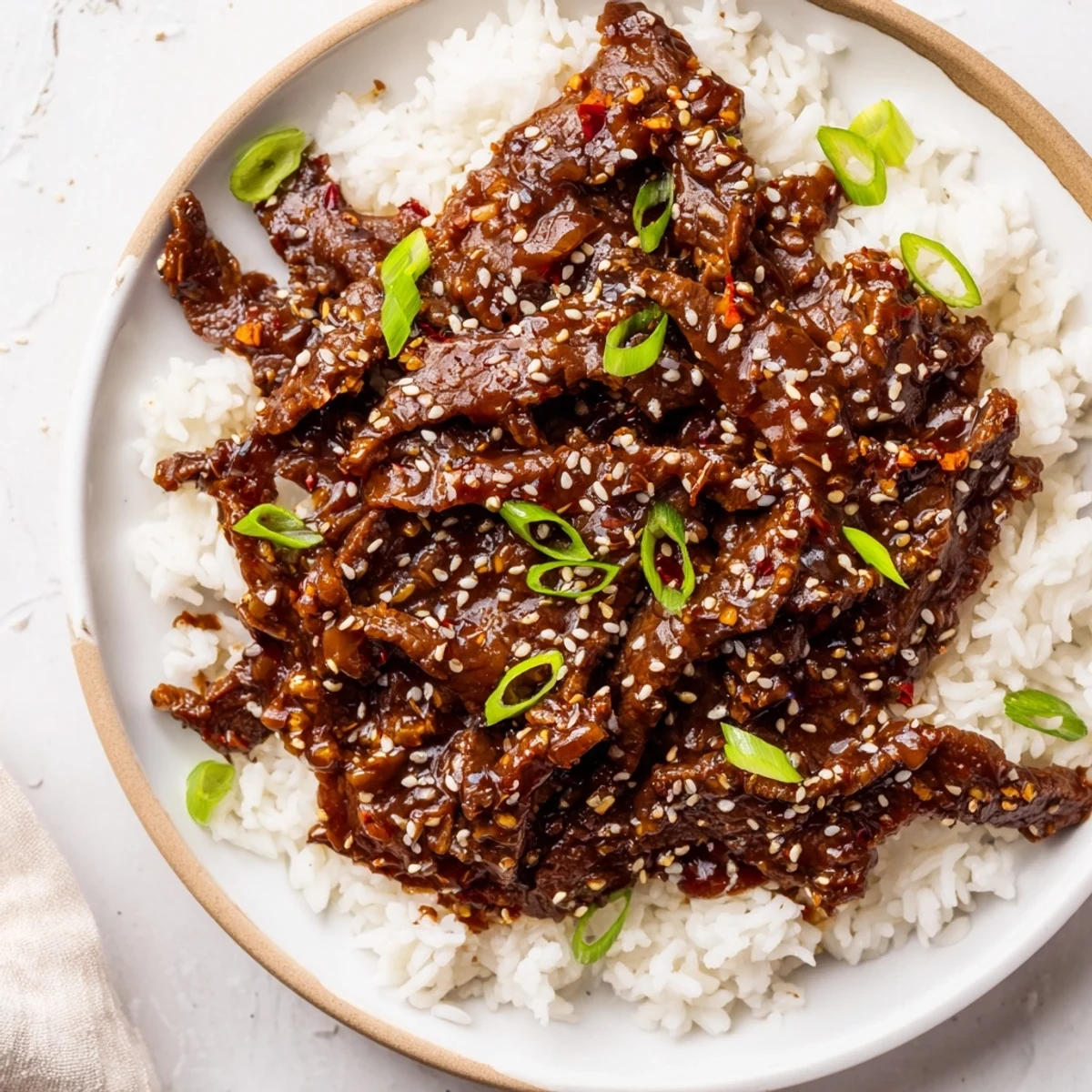 Slow-cooked Ultimate Slow Cooker Mongolian Beef slices glisten in a rich brown sauce, garnished with green onions and sesame seeds served over fluffy white rice.
