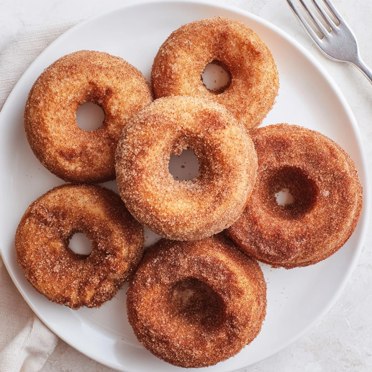 A close-up of Delicious Baked Cinnamon Sugar Donuts You Cant Resist, glistening with buttery cinnamon sugar on a marble counter next to a mug of hot coffee.