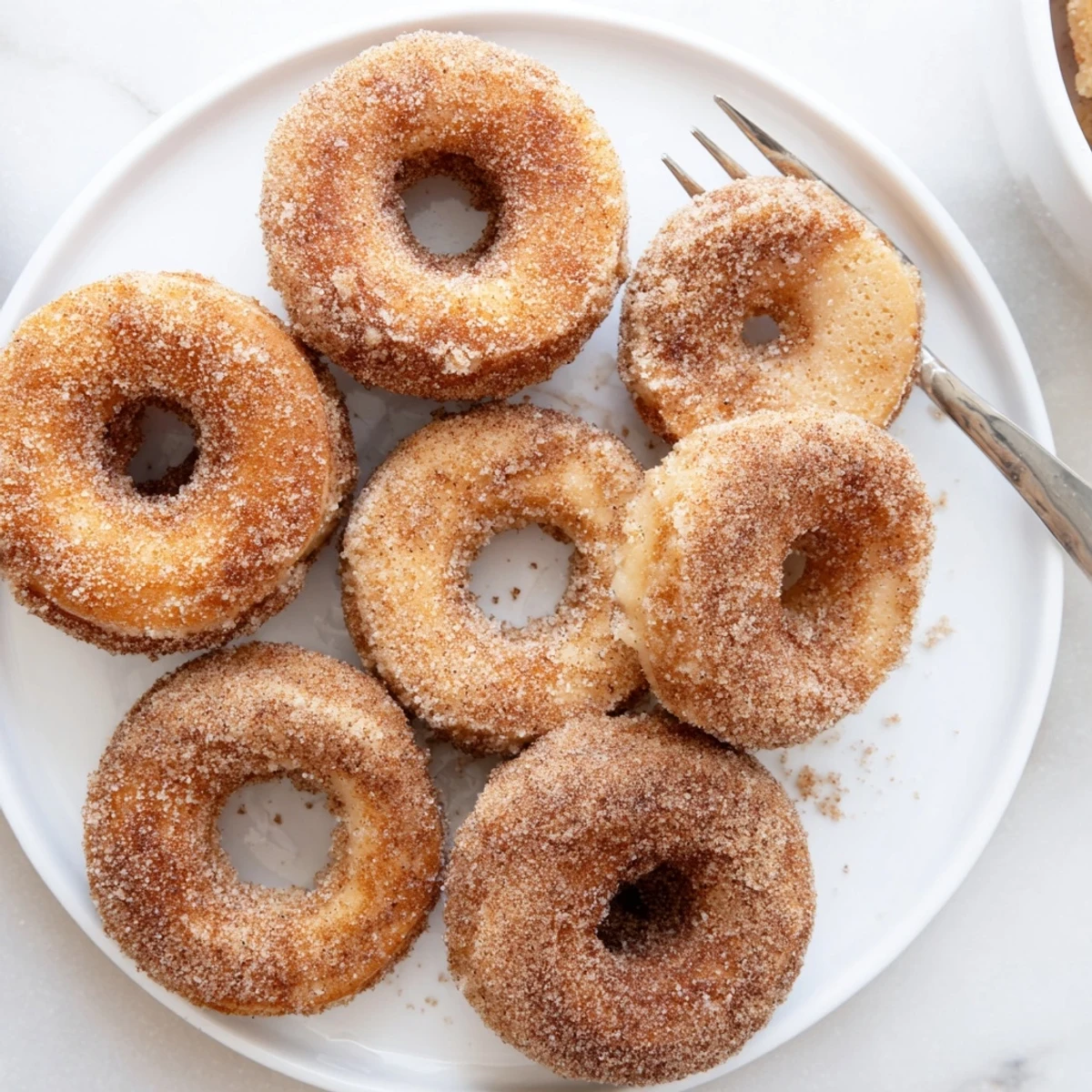 Golden Delicious Baked Cinnamon Sugar Donuts You Cant Resist stacked on a white plate with a cozy breakfast setting and a steaming cup of hot chocolate.