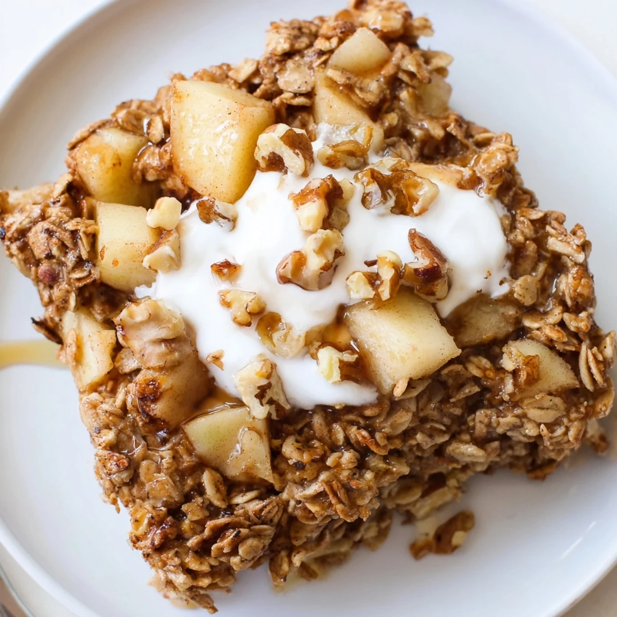 A cozy square of Baked Apple Oatmeal With Greek Yogurt, topped with a creamy dollop and chopped walnuts.