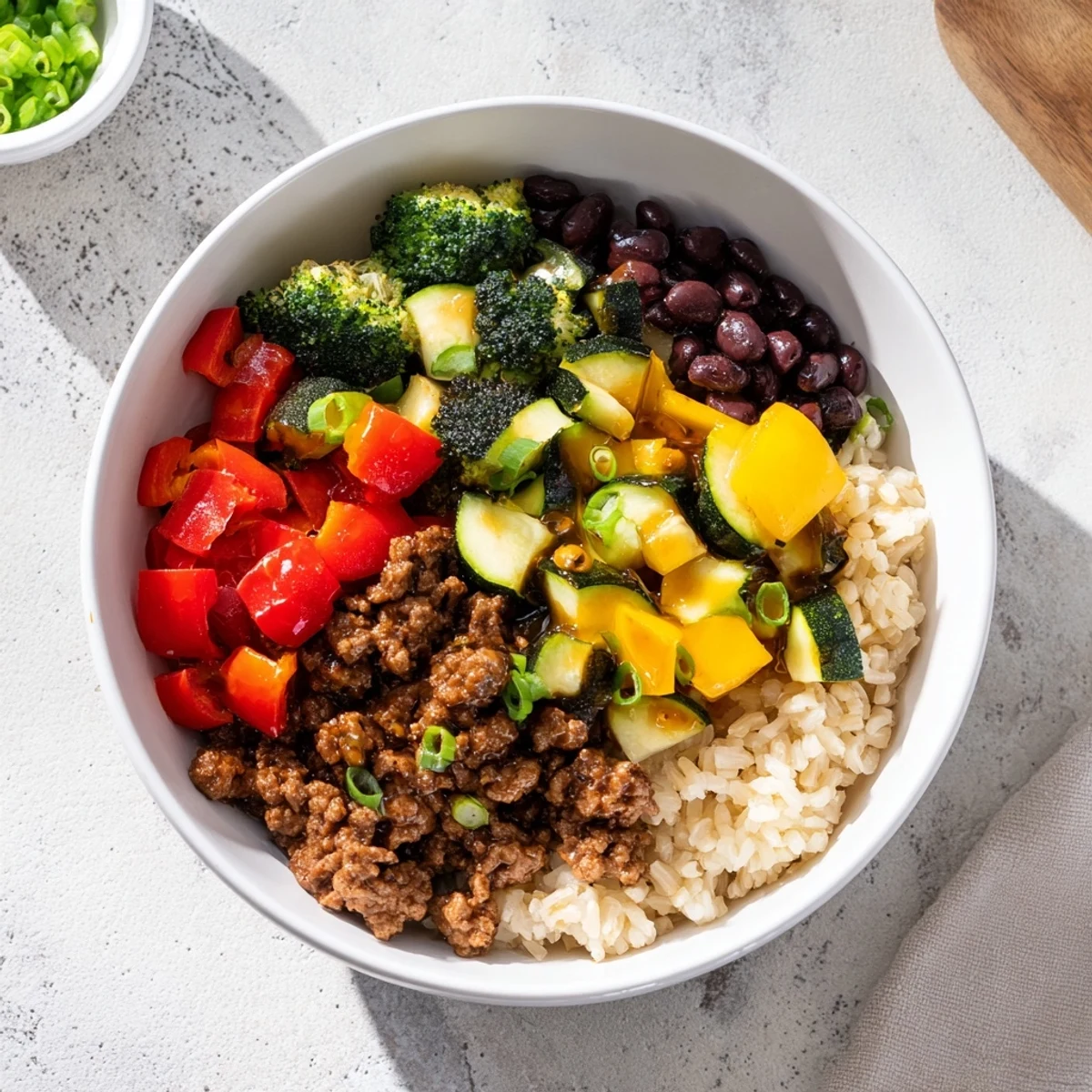 A bowl of Viral Hot Honey Ground Beef Bowl with rice and black beans, garnished with green onions.