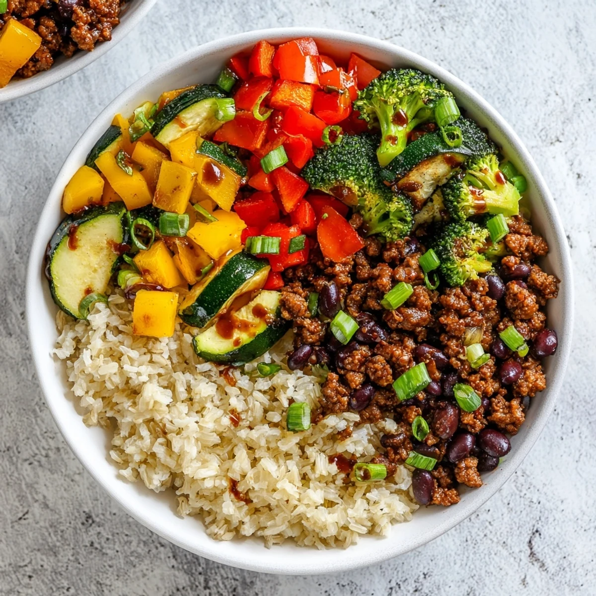 Roasted vegetables and spiced ground beef in a bowl topped with hot honey drizzle and avocado slices.