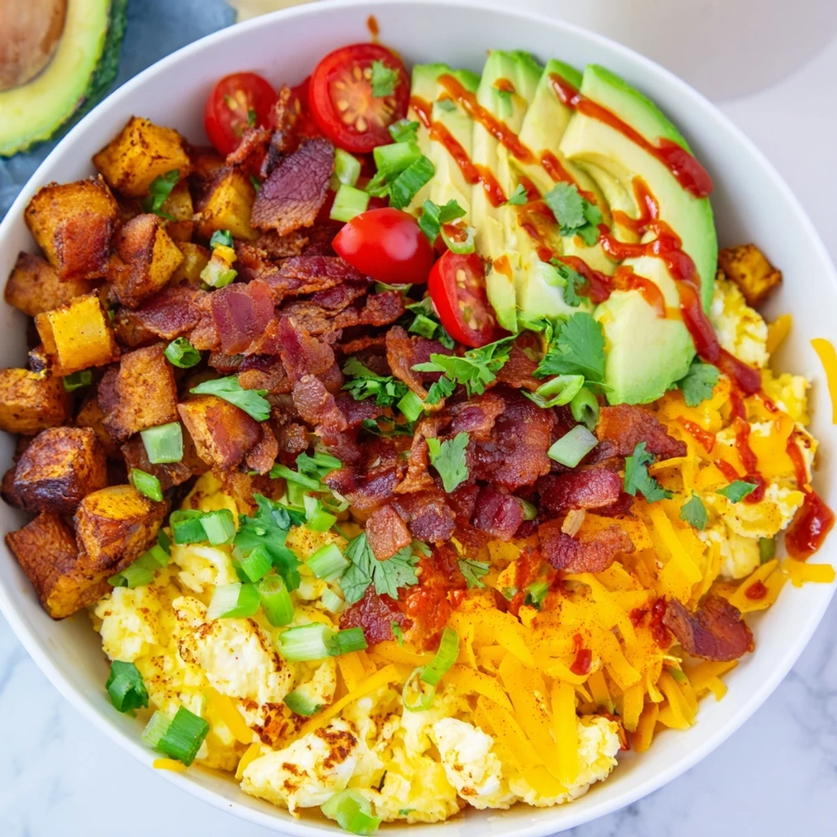 Crispy roasted potatoes, scrambled eggs, and melted cheddar cheese in a Loaded Breakfast Bowl topped with avocado and bacon.