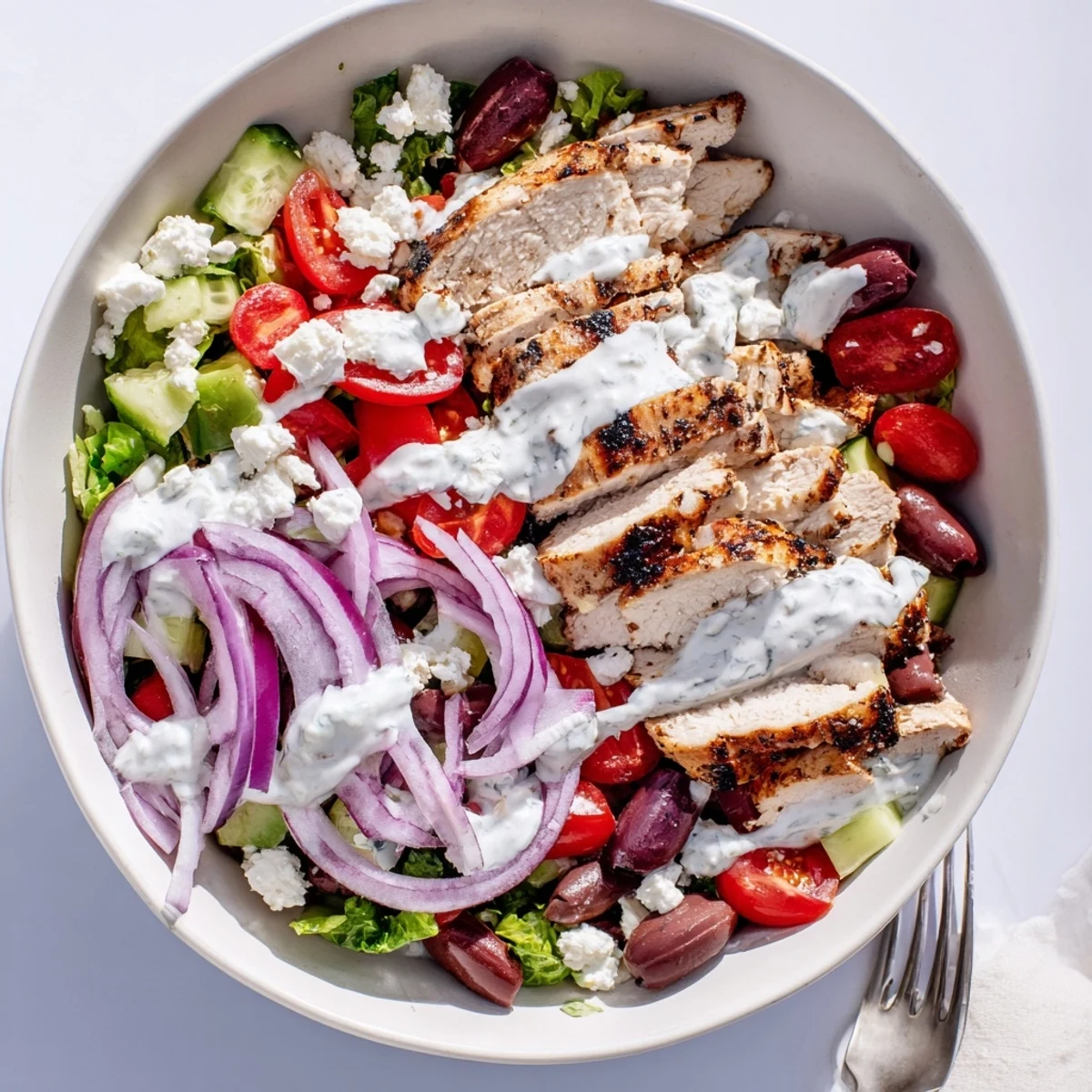 Grilled chicken slices topped with creamy tzatziki dressing on a bed of fresh mixed greens, tomatoes, and feta.