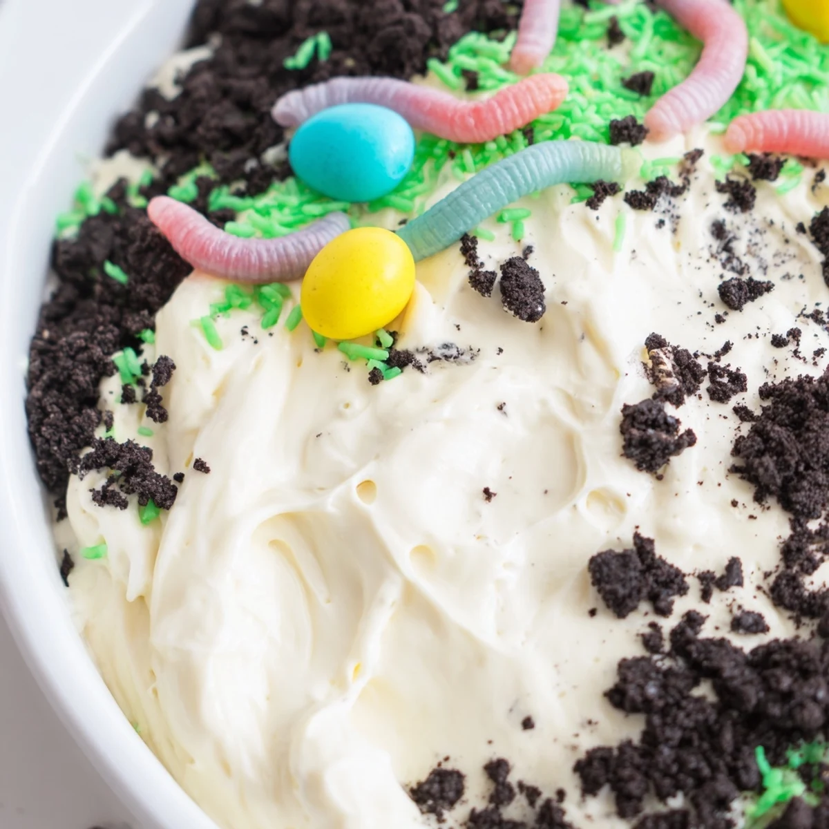 Close-up of Easter Dirt Cake Casserole with creamy layers, cookie crumbs, and gummy worms on a festive spring table.