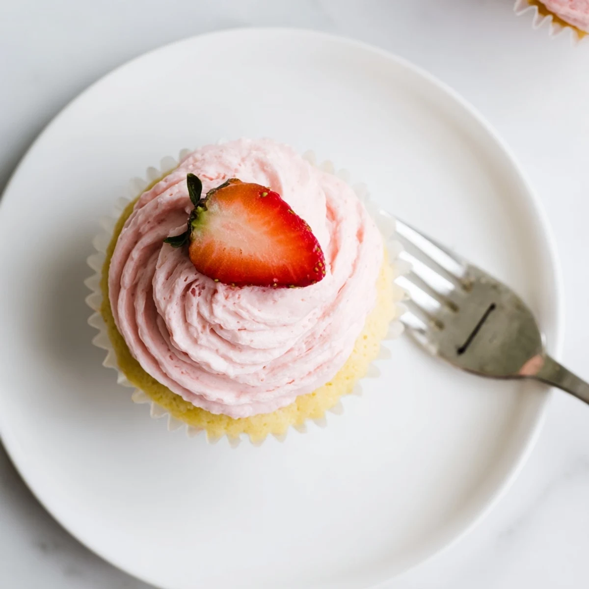 Spring dessert featuring bright lemon cupcakes swirled with creamy homemade strawberry buttercream on white plate