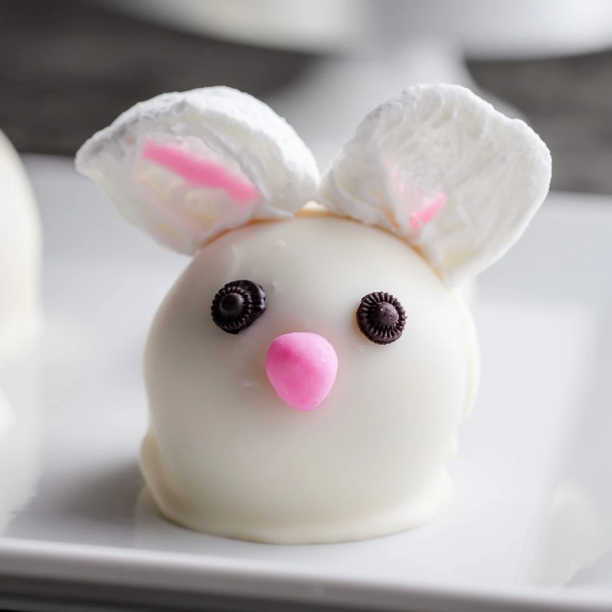 White chocolate bunny Oreo balls decorated with pink ears and fluffy marshmallow tails on a parchment-lined baking sheet
