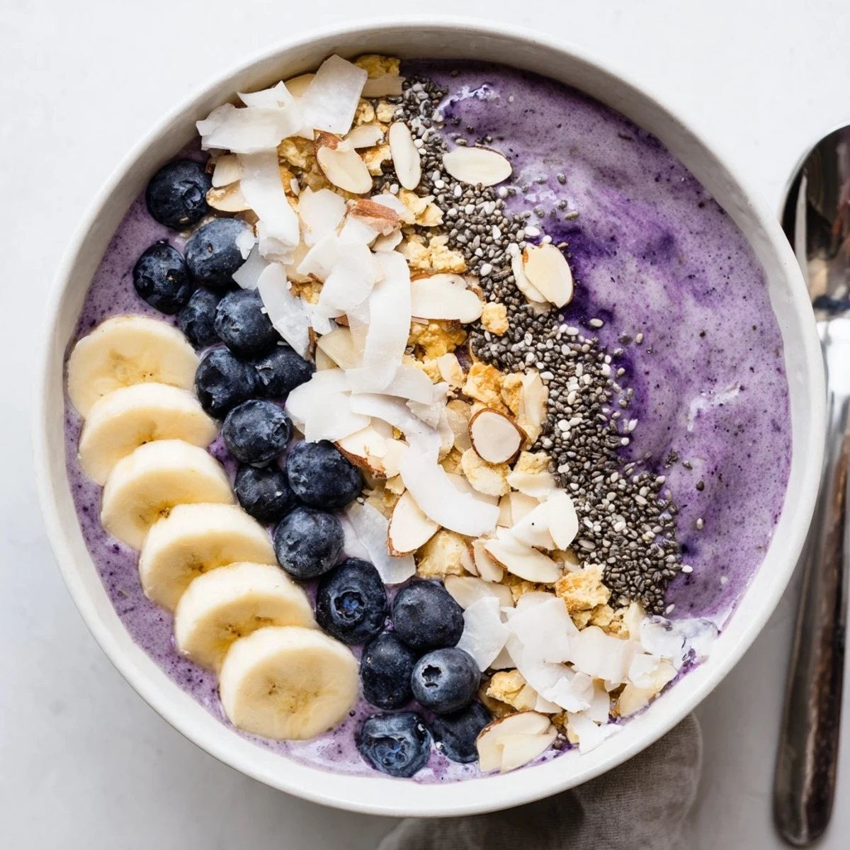Creamy blueberry smoothie bowl with Greek yogurt topped with fresh berries, granola, coconut flakes, and sliced almonds