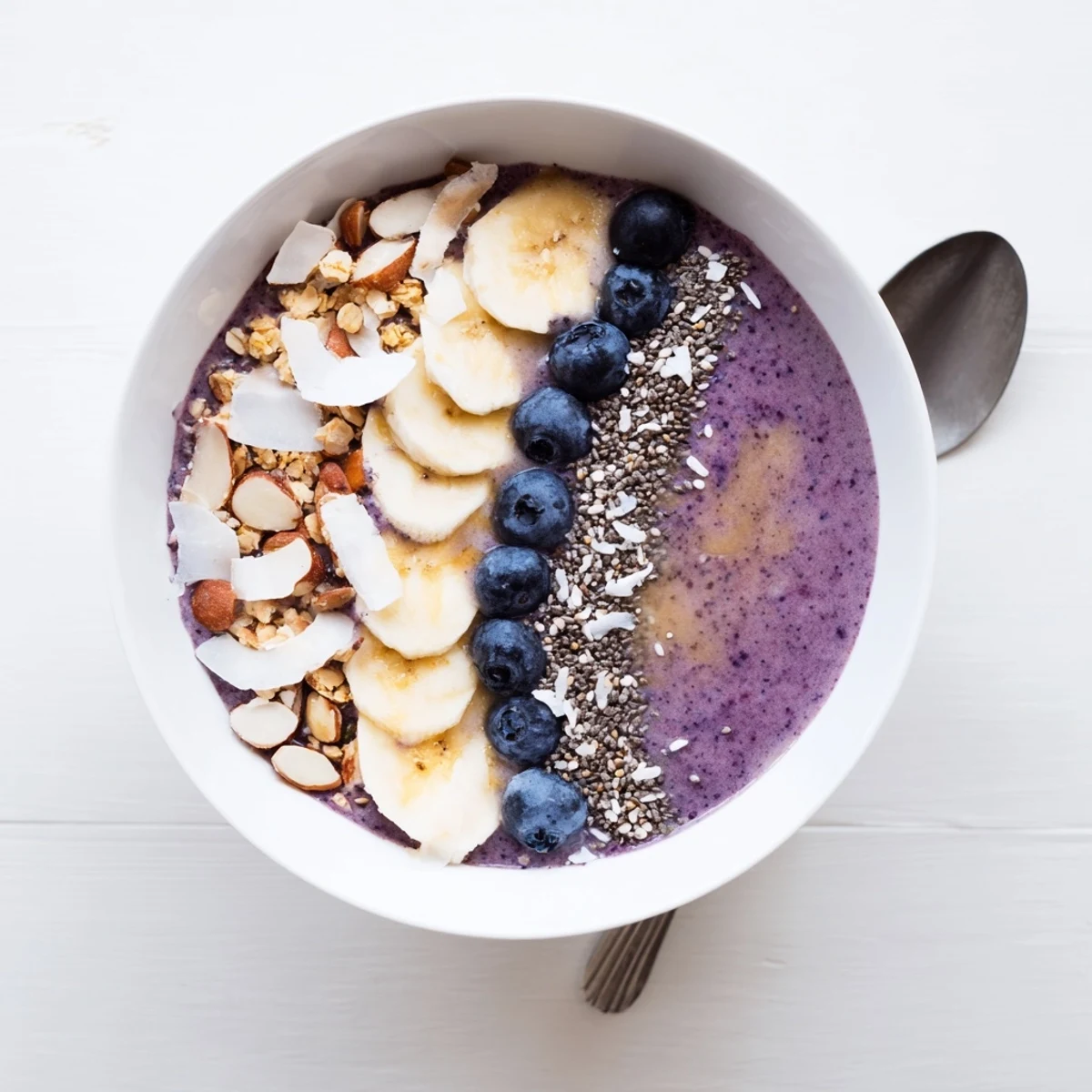 Thick purple smoothie bowl made from frozen blueberries and Greek yogurt, garnished with fresh fruit and nutty toppings