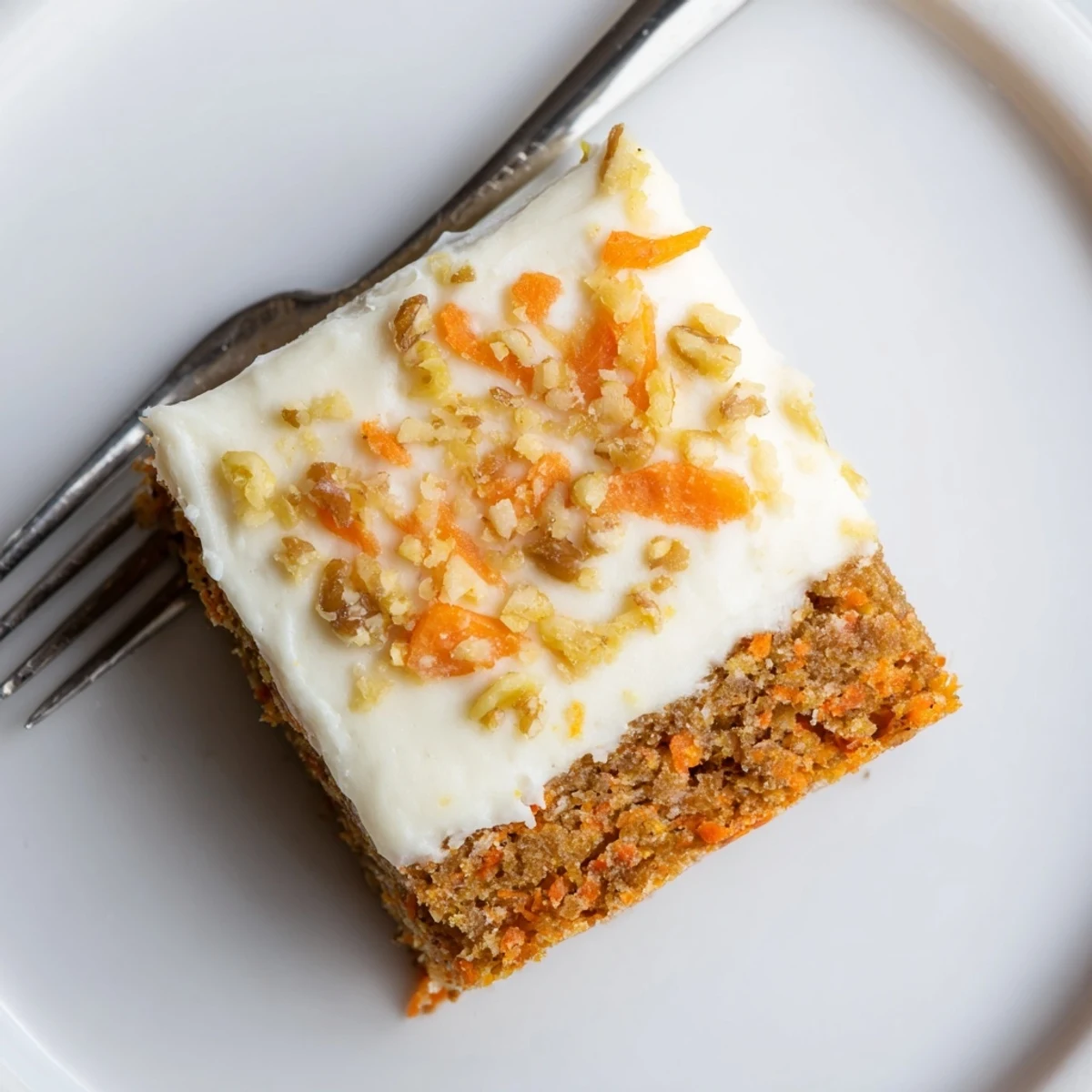 Decadent carrot cake bars with cream cheese frosting topped with chopped walnuts on a white plate