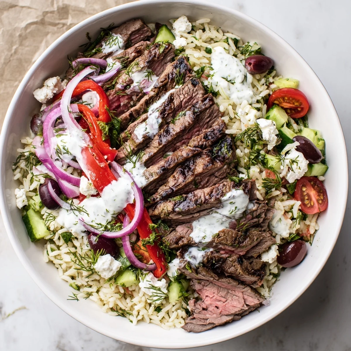 Protein-packed Mediterranean steak bowl arranged with perfectly grilled flank steak, crisp veggies, creamy feta, and zesty yogurt drizzle