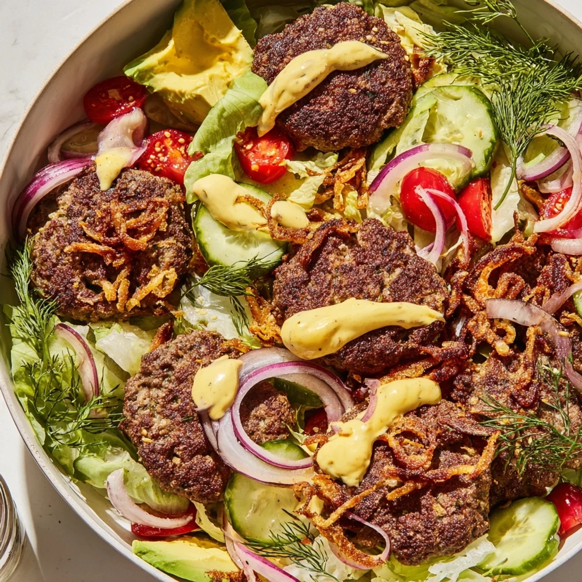 Golden smash burger bowl featuring crispy beef patties over fresh greens with tangy pickles and creamy sauce