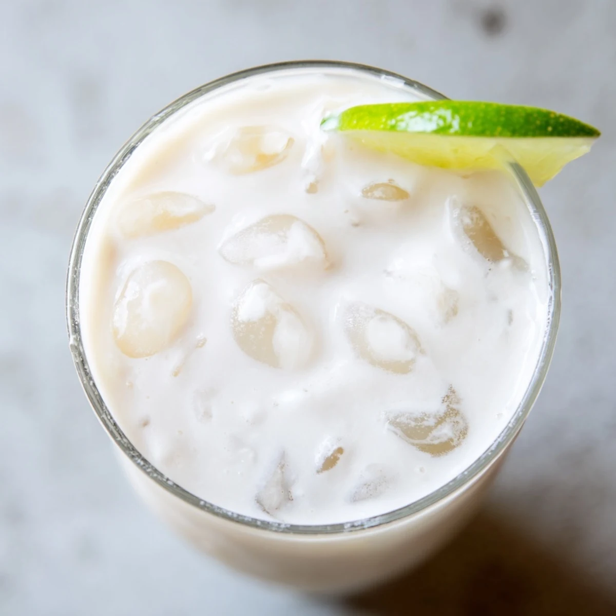 Tall glass of creamy coconut lychee iced drink garnished with fresh mint leaves and lime slices