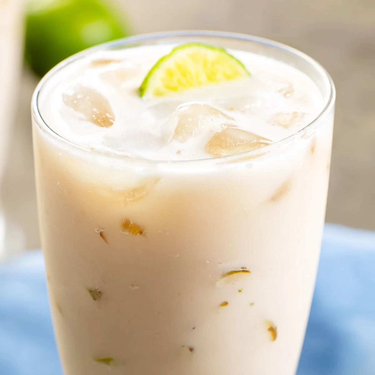 Refreshing coconut lychee iced drink poured over ice with whole lychee fruit floating in a clear glass