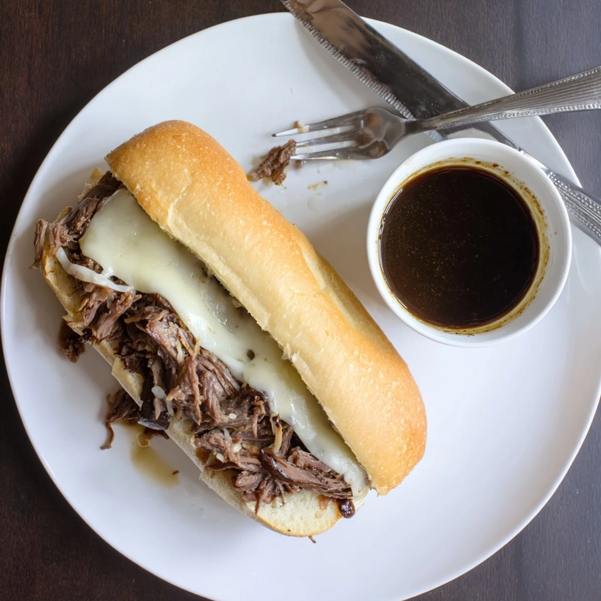 Juicy beef Crockpot French Dip Sandwiches piled on crusty rolls alongside small bowls of rich beef broth for dipping