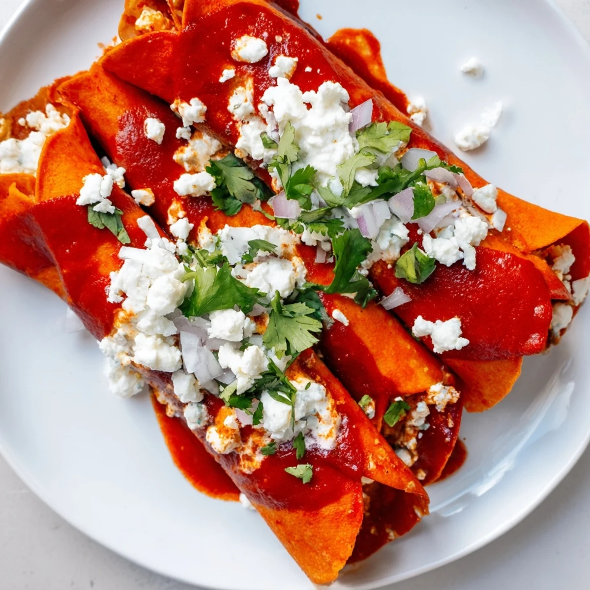 Entomatadas folded in half and covered in rich red tomato sauce with crumbled cheese.