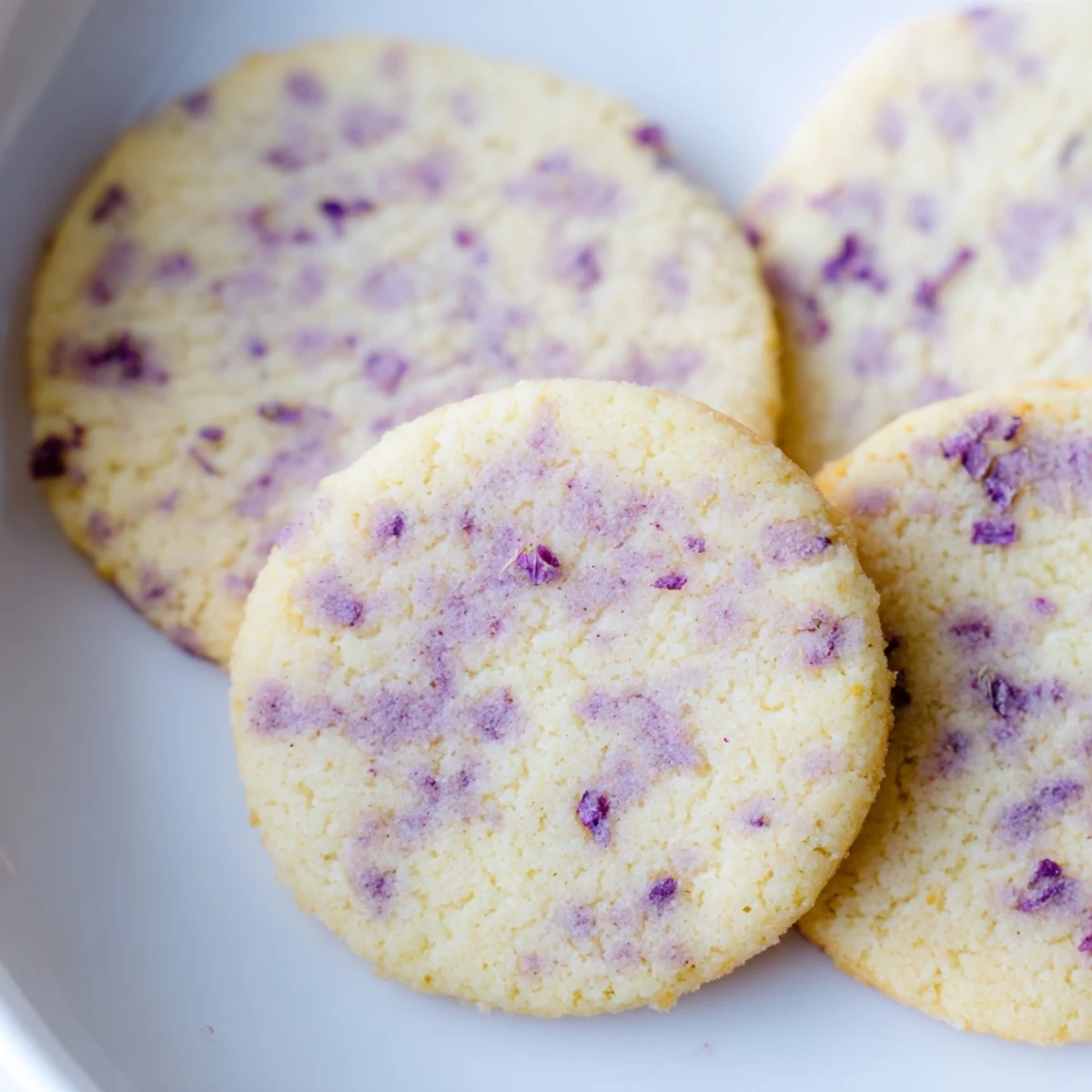 Buttery lilac sugar cookies arranged on a rustic white ceramic serving plate