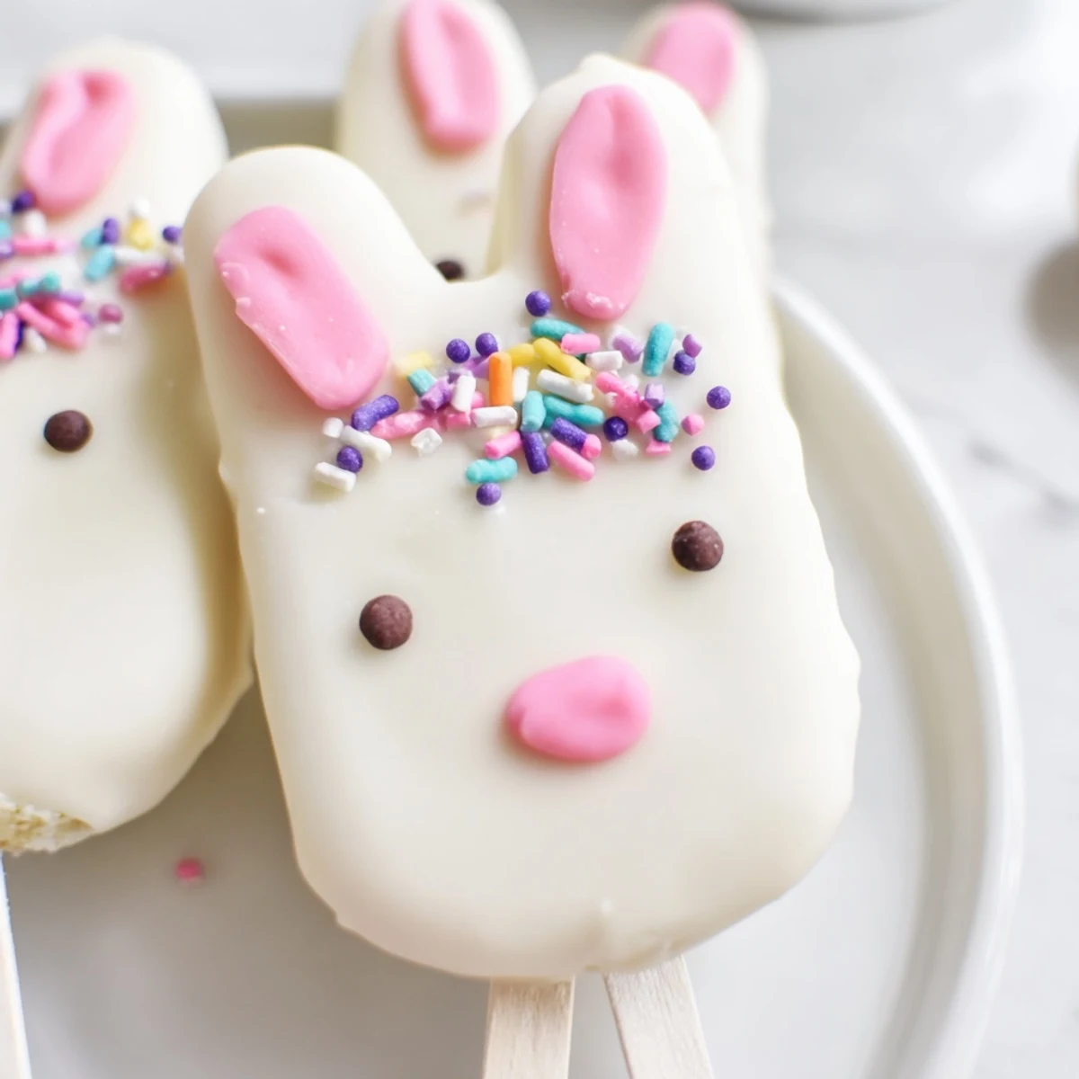 Adorable white chocolate bunny cakesicles with candy eyes on a wooden serving board