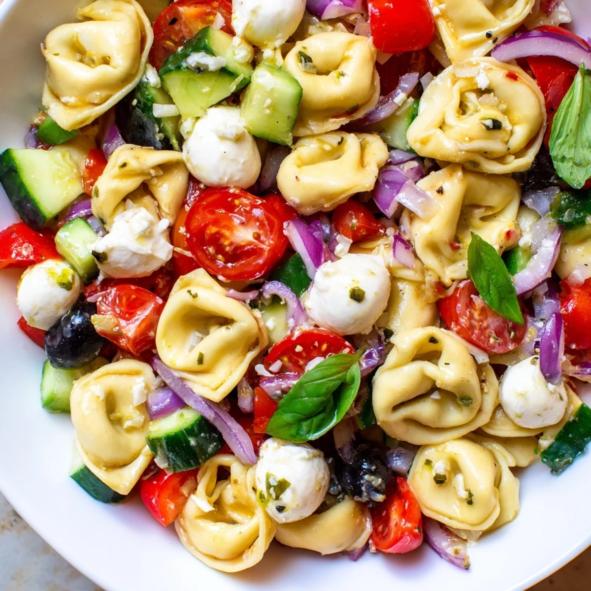 Colorful tortellini salad with ripe cherry tomatoes, crisp cucumber, and zesty Italian vinaigrette in a white serving bowl