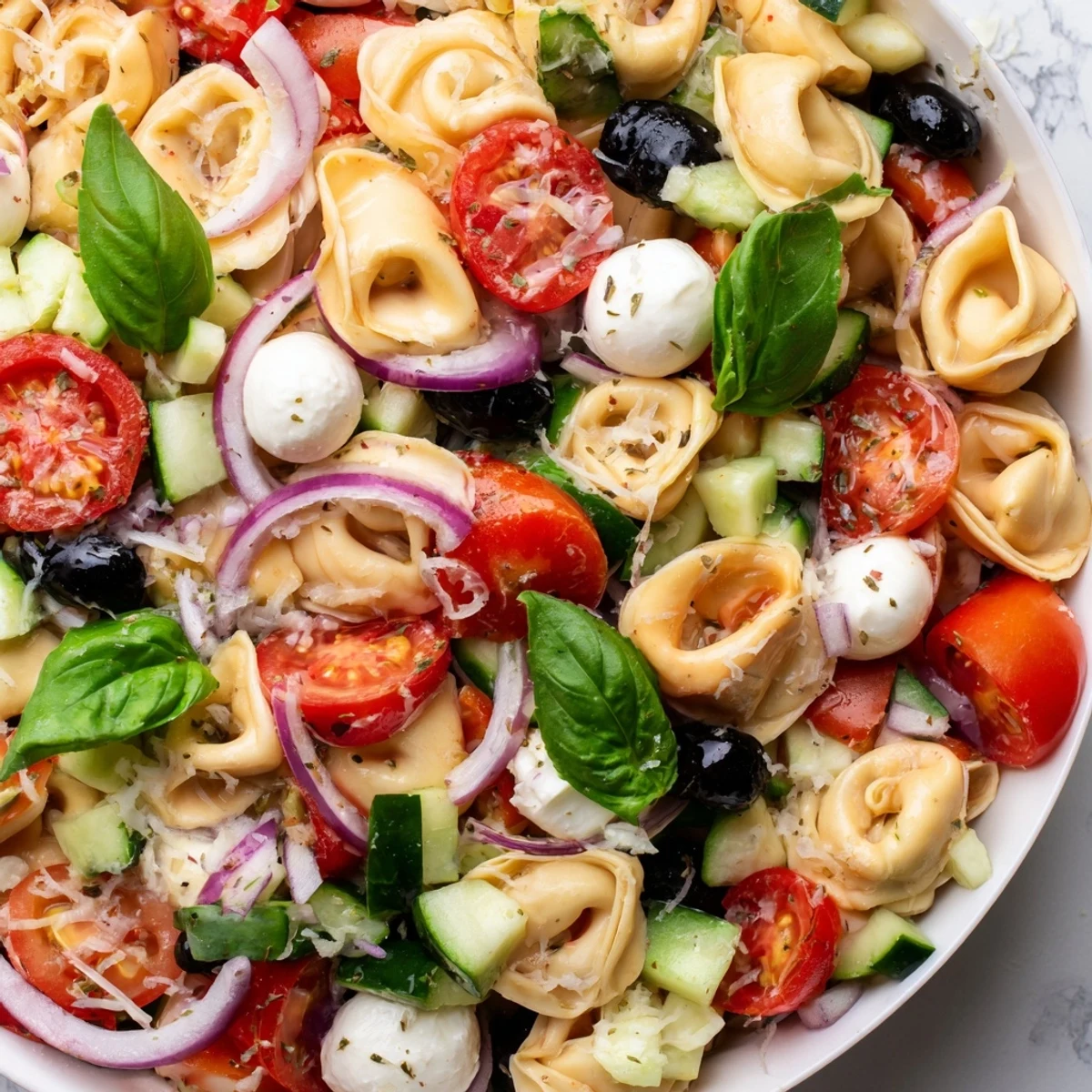 Cheese tortellini salad tossed with mozzarella, olives, and fresh basil glistening under tangy herb dressing