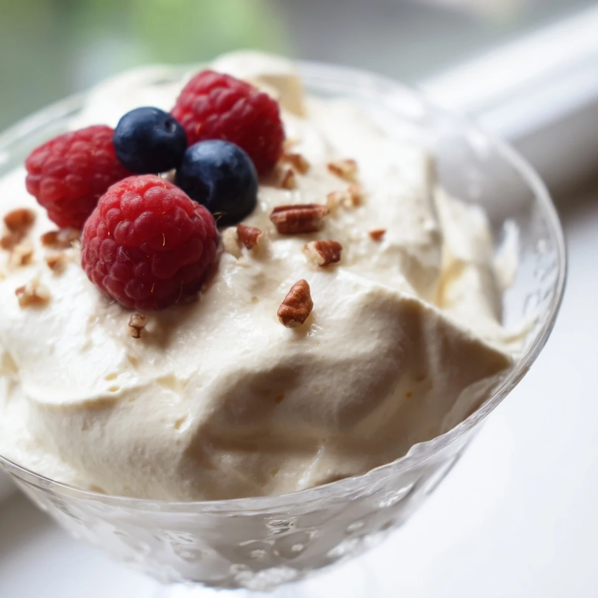 Creamy keto cheesecake fluff spooned into glasses topped with fresh red berries and chopped nuts