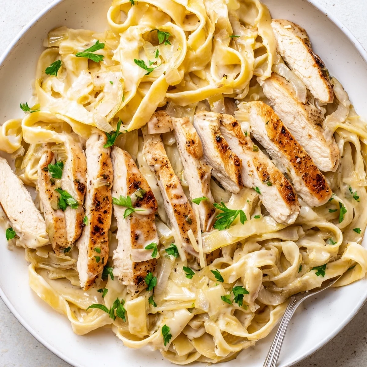 Creamy Garlic Chicken Pasta plated with parsley, steaming, silky sauce coating fettuccine.