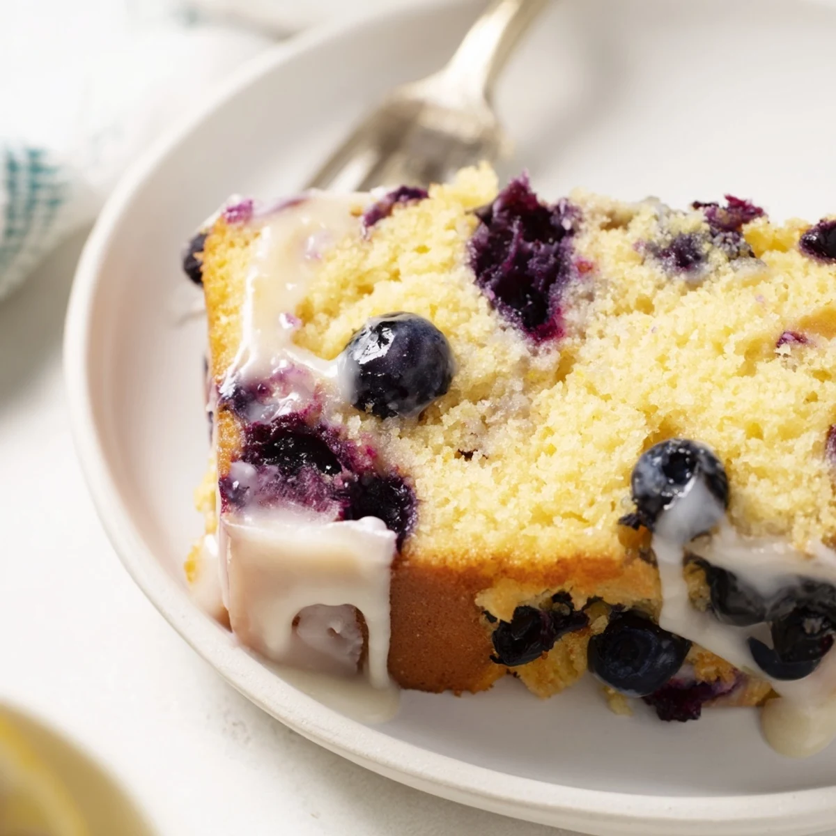 Moist lemon blueberry cake drizzled with tangy glaze on a white serving plate