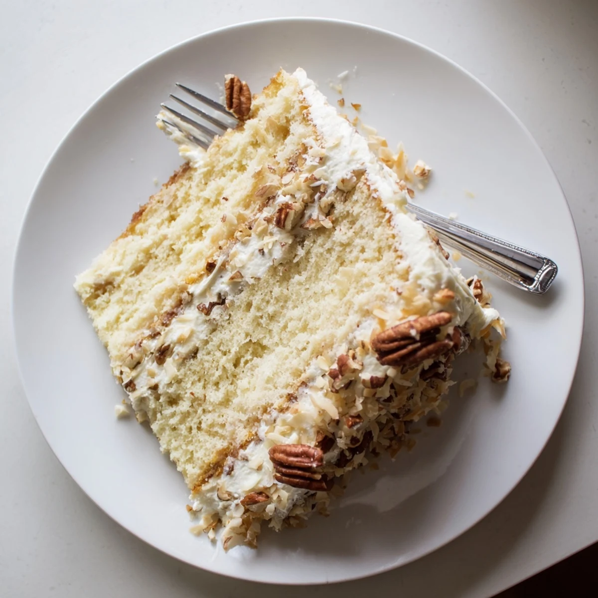 Slice of Quick Italian Cream Cake featuring creamy frosting and crunchy pecan garnish