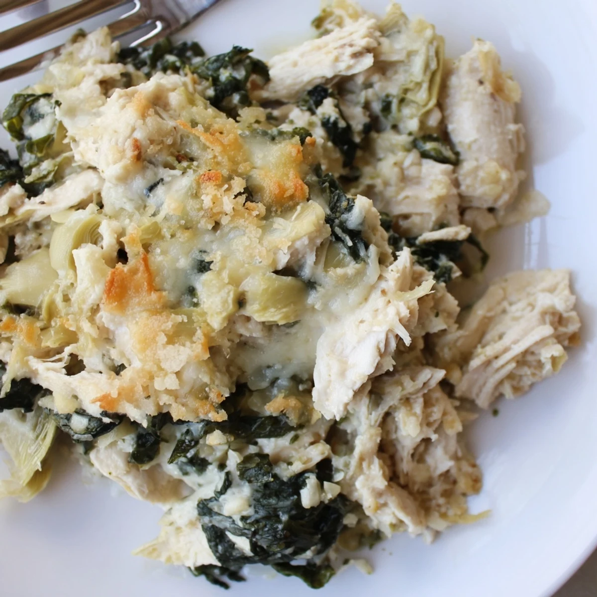 Creamy spinach and artichoke chicken casserole with melted mozzarella and golden breadcrumb topping bubbling in a baking dish