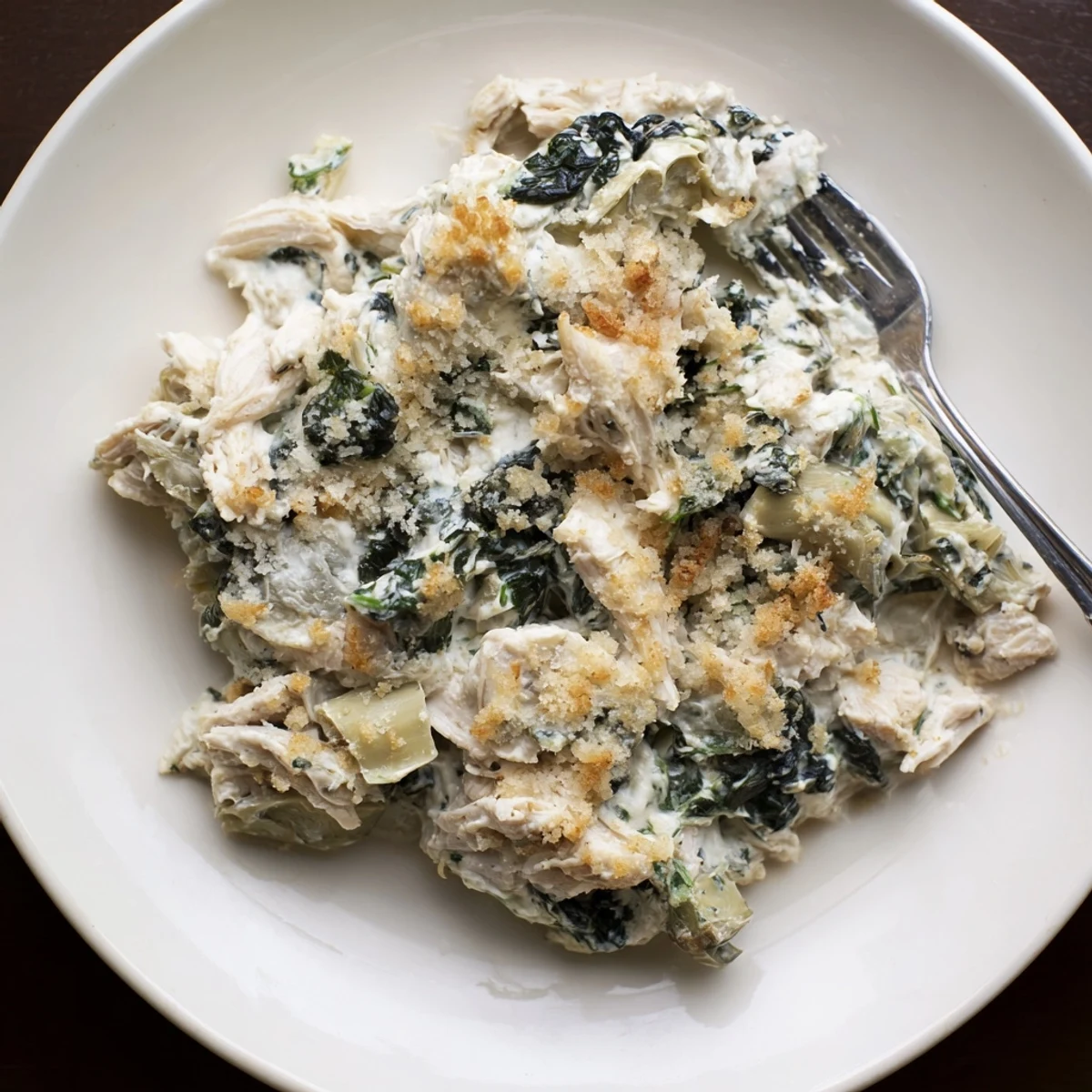 Golden bubbly spinach and artichoke chicken casserole fresh from the oven with gooey cheese and savory vegetable-filled creamy sauce