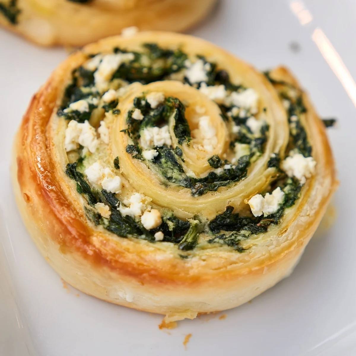 Golden gluten free spinach and feta pinwheels baked to flaky perfection on a white serving plate