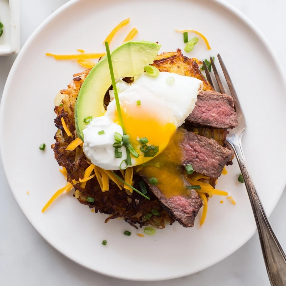 Loaded Steak Egg Hash Brown Stacks with runny yolk, melted cheddar, avocado slices