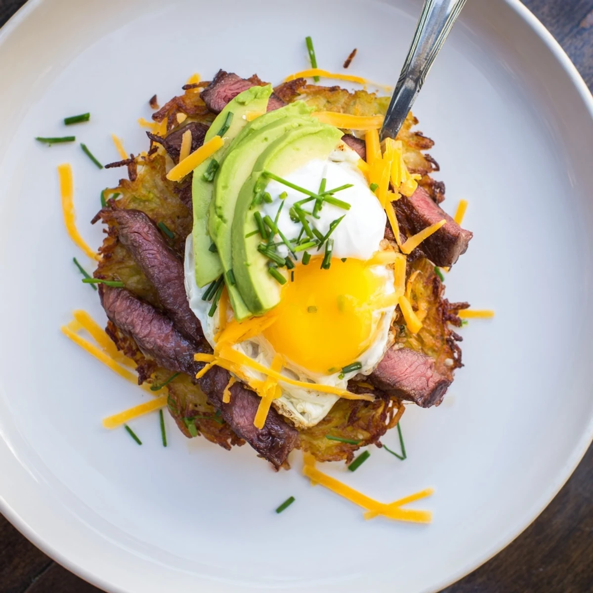 Seared steak atop Loaded Steak Egg Hash Brown Stacks, garnished with fresh chives