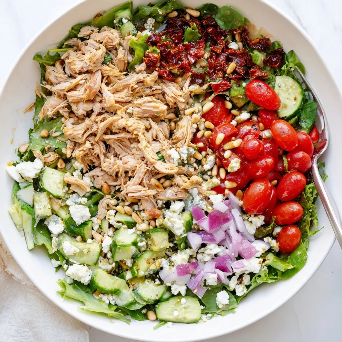 Protein-packed sun-dried tomato chicken salad bowl with mixed greens and toasted pine nuts